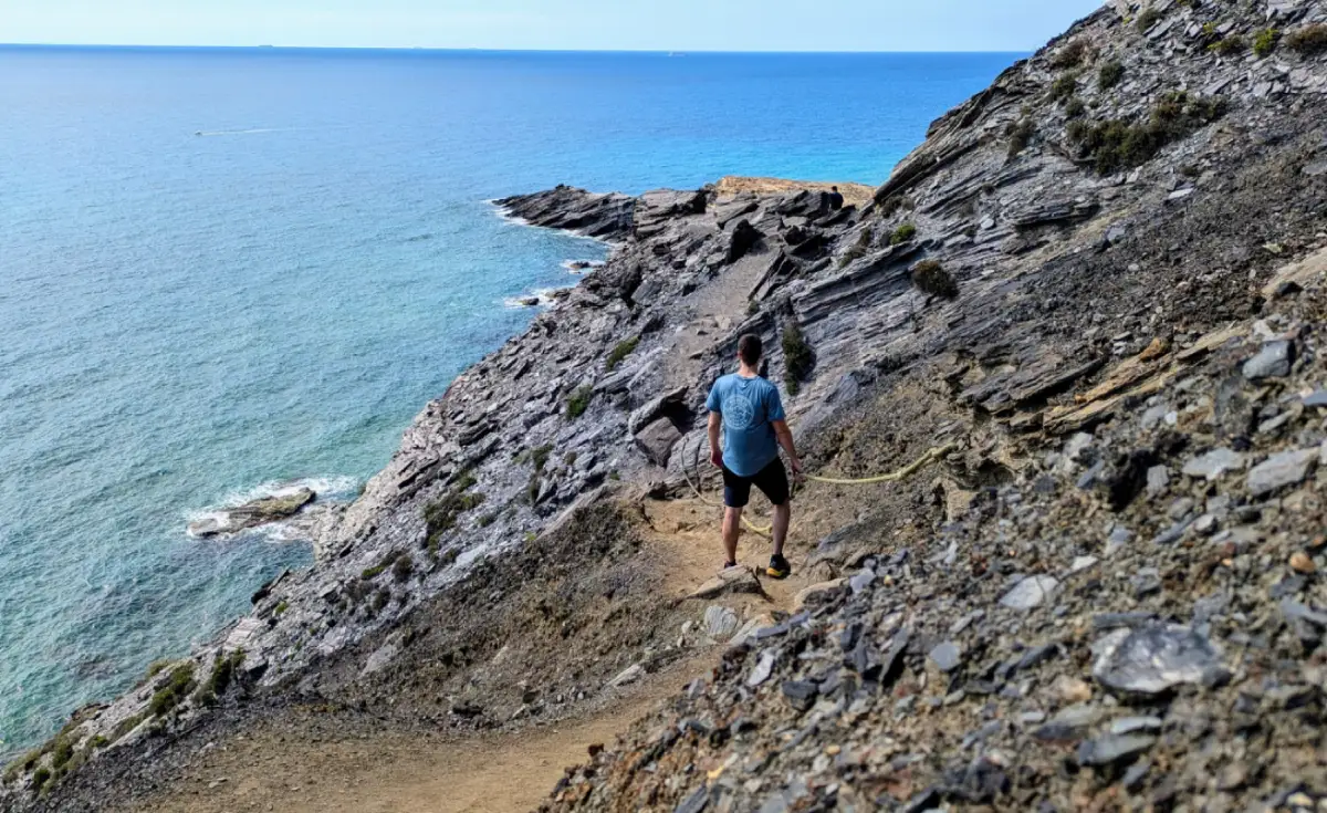persona caminando por acantilado con la playa de fondo